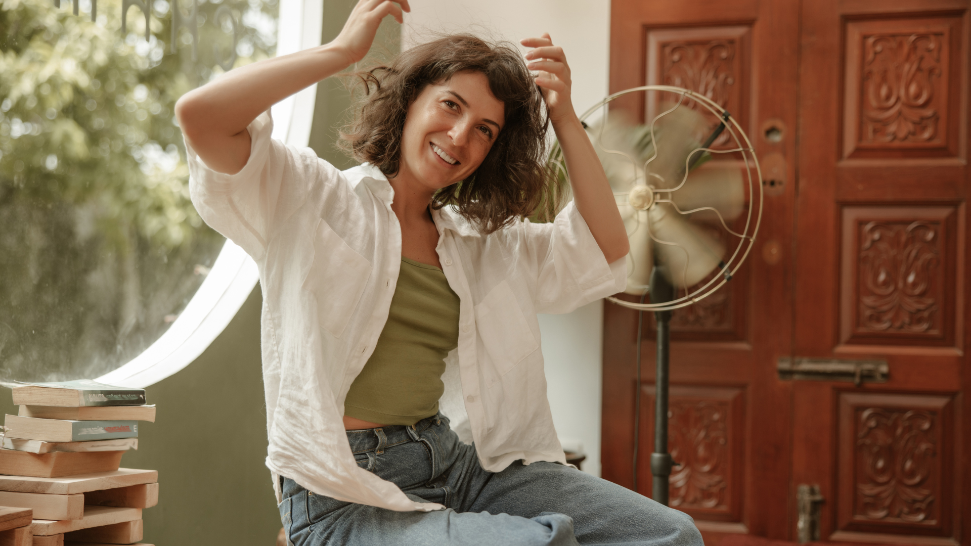 Mulher usando ventilador em ambiente residencial para se refrescar em dias quentes, representando conforto térmico e consumo consciente de energia.