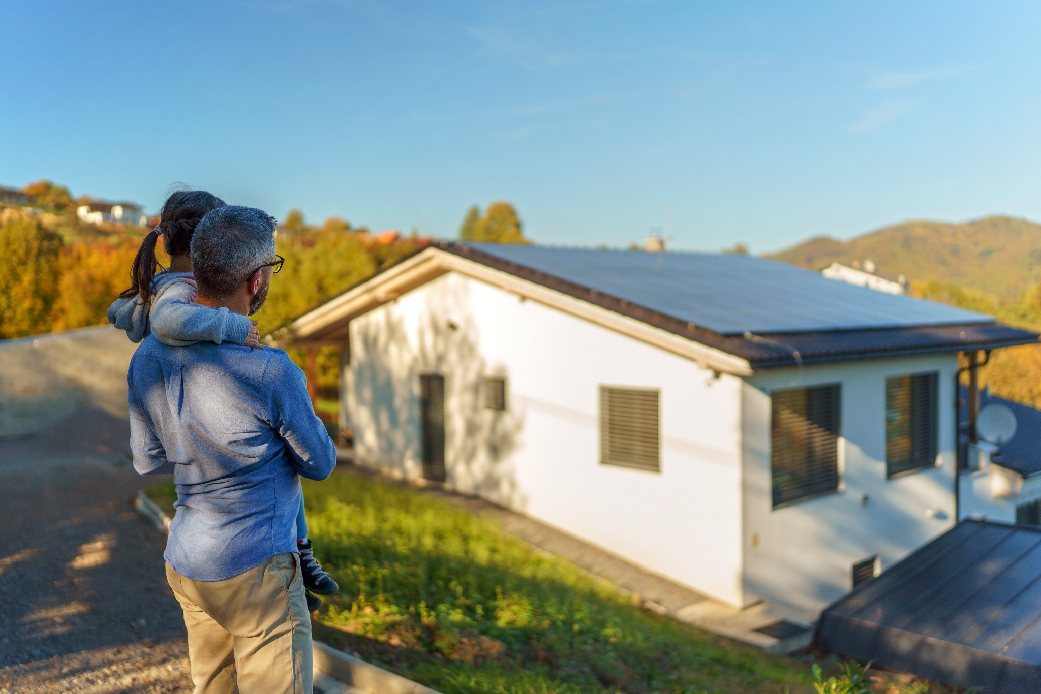 Adulto com criança olhando casa com painéis solares.