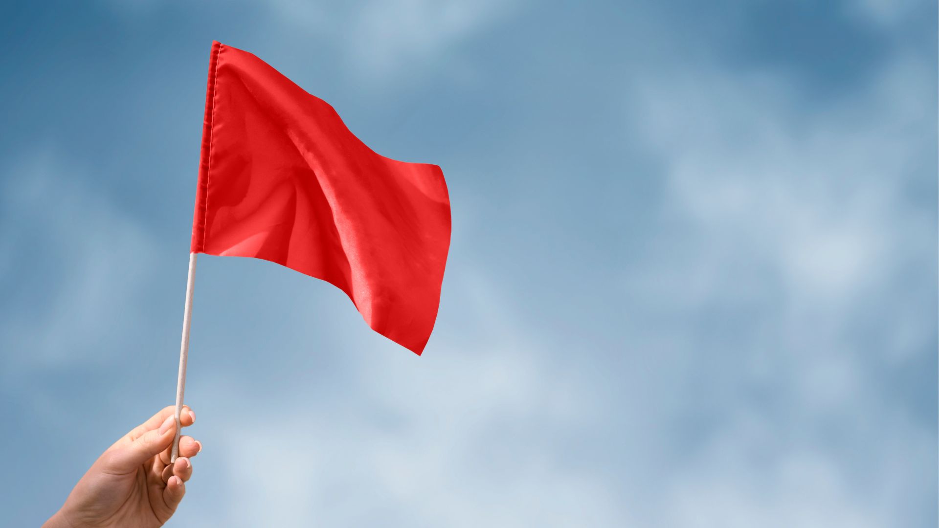 mão segurando uma bandeira vermelha ao ar livre, simbolizando o aumento de custos das bandeiras tarifárias de energia