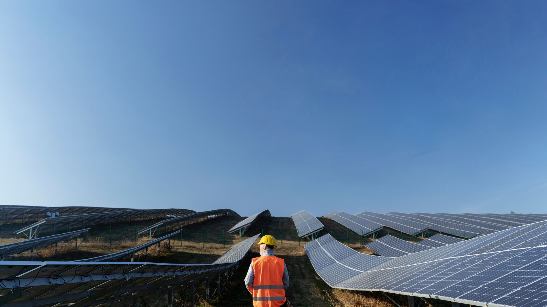 Técnico observa fileiras de painéis solares em uma usina fotovoltaica.