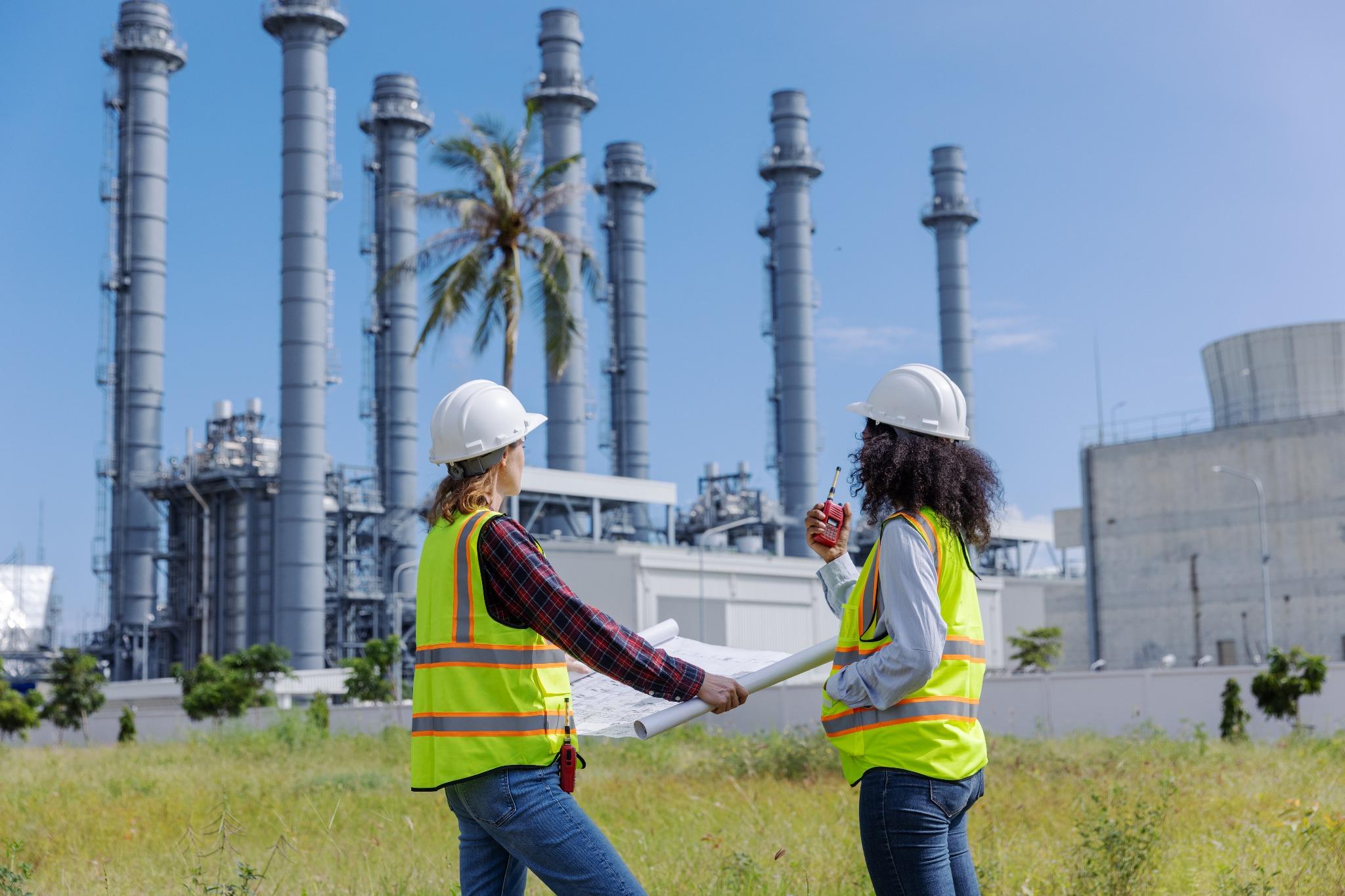 Engenheiras analisam plantas em frente a usina termoelétrica.