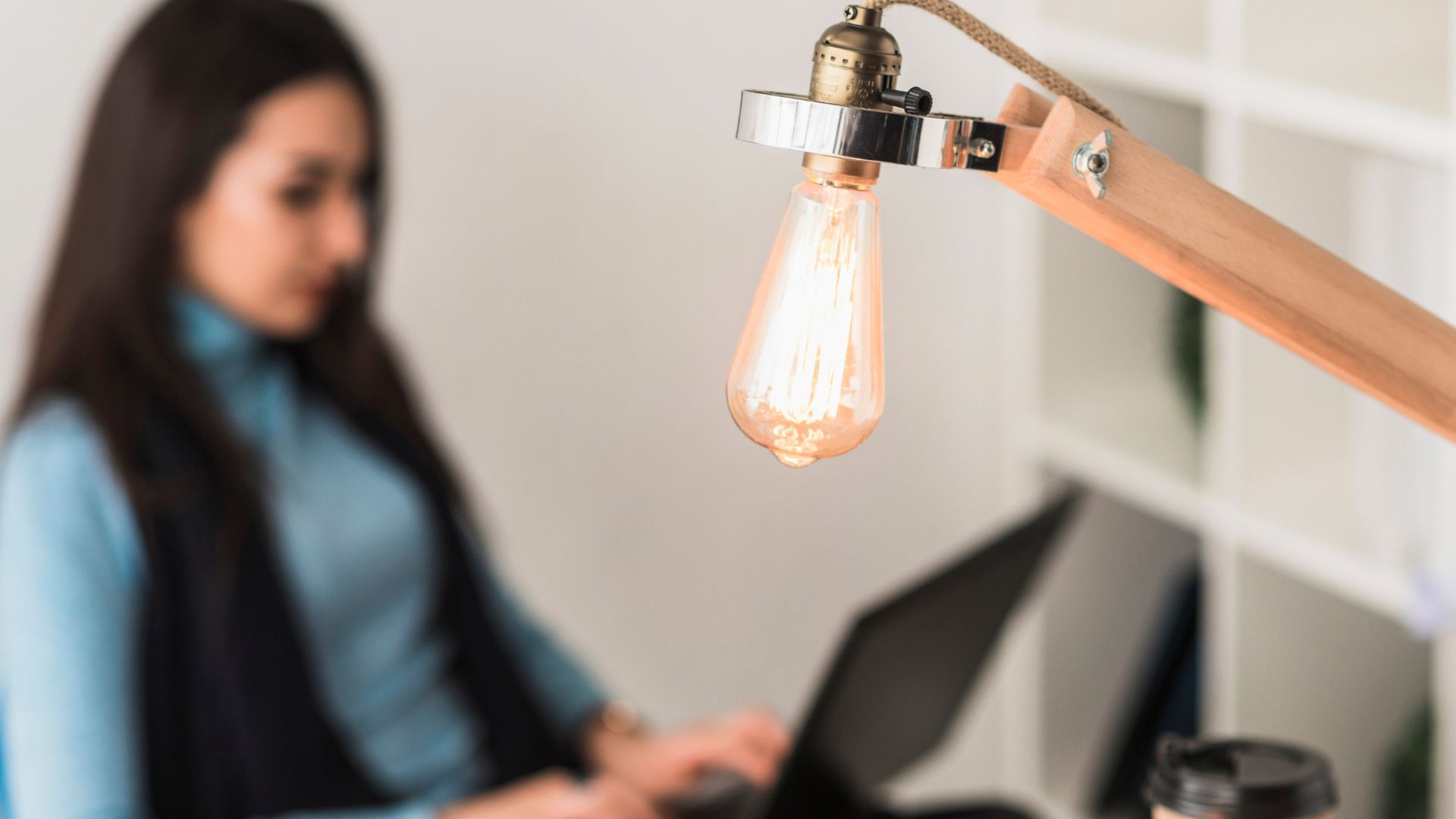 Mulher trabalhando ao lado de uma lâmpada acesa, representando consumo de energia e a busca por alternativas como energia solar por assinatura.