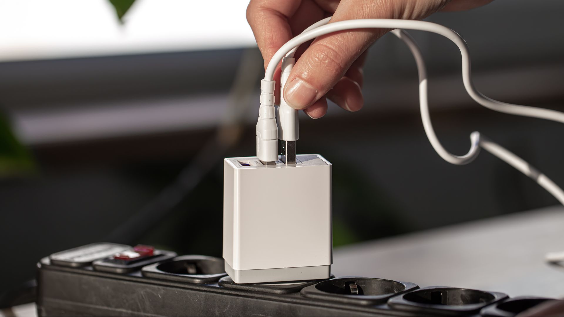 Mão conectando carregador de celular na tomada mostrando consumo de energia elétrica em ambiente doméstico.